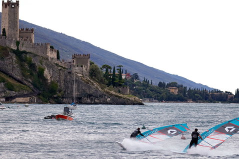 Duotone Warp Fin race sail during windsurfing on a lake with castle and mountain backdrop