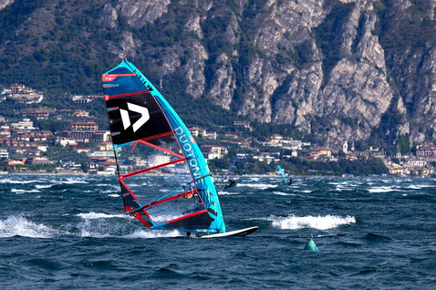 Duotone Warp_Fin race sail 7.8m² during windsurfing on a lake with mountain backdrop