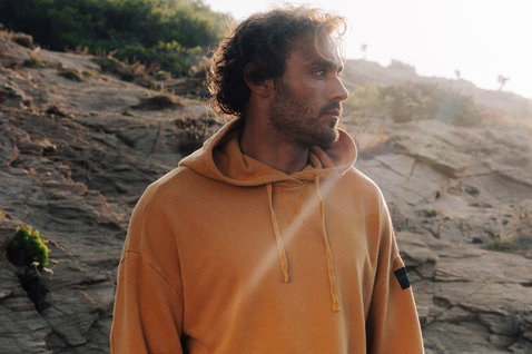Duotone Hoody True Fade Out homme sweat à capuche en pose debout sur colline côtière rocheuse