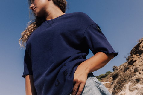 T-shirt à manches courtes Duotone Sweat Tee SS True Fade Out unisexe en bleu marine en pose sur une falaise côtière rocheuse