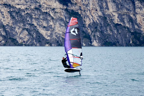 Duotone Falcon Foil D/LAB foil board during wing foiling on a lake with rocky cliff background