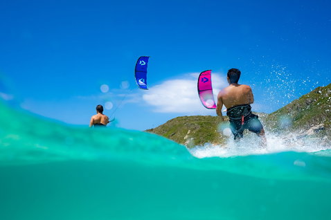 Duotone Evo SLS LEI kite durante il kitesurf su una spiaggia tropicale con collina verde