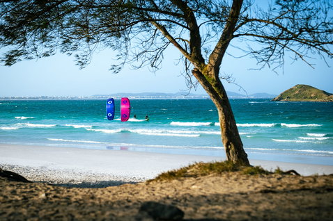 Duotone Evo SLS LEI kite durante il kitesurf sull'oceano su una spiaggia sabbiosa con isola rocciosa