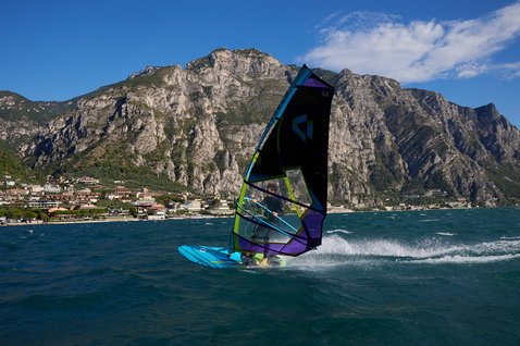 Duotone Eagle Windsurf Board beim Windsurfen auf einem Alpensee mit Bergkulisse und Küstenstadt