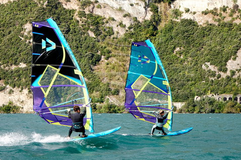 Duotone E_Pace freeride sail 8.8m² during freeride windsurfing on an alpine lake with rocky cliffs and forested hillside