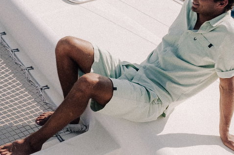 Duotone Apparel Shorts True Beach men short de plage en vert sauge au repos sur le pont d'un catamaran avec vue sur l'océan