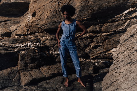 Duotone Apparel Jumpsuit True tuta donna in posa in piedi su scogliere rocciose costiere in blu denim