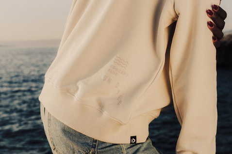 Duotone Sweater CB undyed women Concept Blue pull en écru naturel sur une côte rocheuse au bord de l'océan