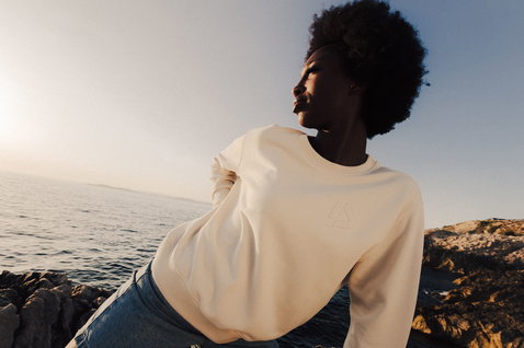 Duotone Apparel Sweater CB Concept Blue sweatshirt femme en pose debout sur une côte rocheuse au bord de l'océan