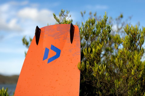 Duotone Gonzales twin-tip kiteboard en orange avec bleu et noir dans un cadre côtier