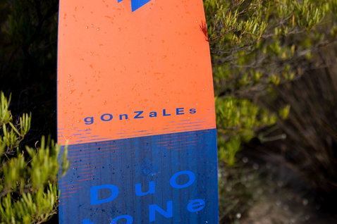 Duotone Gonzales twin-tip kiteboard lors d'une session de kitesurf dans un maquis côtier en orange avec bleu et marine