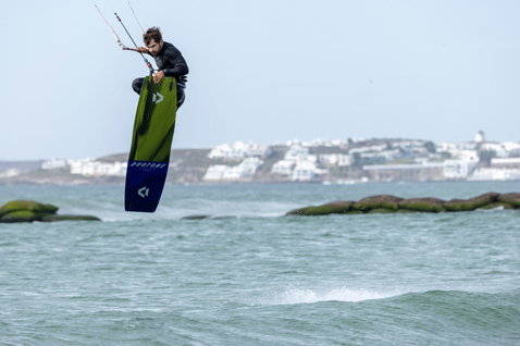Duotone Spike SLS twin-tip kiteboard during kitesurfing on an ocean coast with rocky shoreline and whitewashed town in background