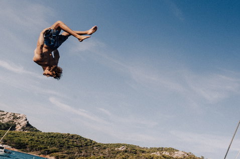 Duotone DT Originals boardshorts 17 pouces en bleu marine foncé lors d'un saut acrobatique sur une baie méditerranéenne