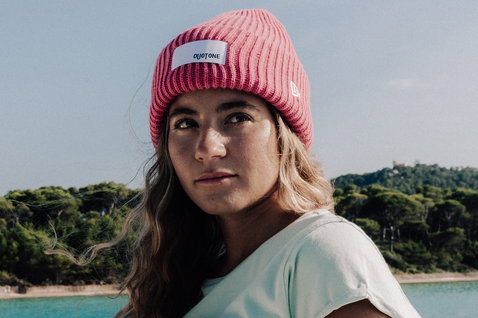 Duotone New Era Logo beanie en rose corail porté par une femme au bord de la côte