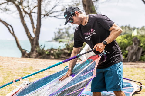 Duotone cap while rigging a windsurf sail at a grassy coastal area with ocean in the background