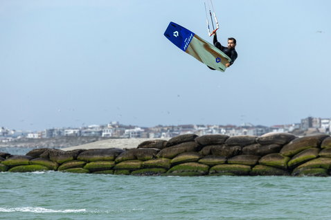 Duotone Spike Concept Blue twin-tip kiteboard during kitesurfing at a coastal beach with stone sea wall