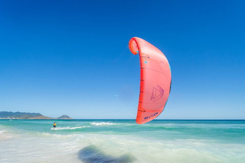 Duotone Evo LEI kite en train de faire du kitesurf sur la plage avec des montagnes en arrière-plan