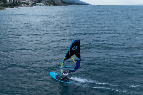 Duotone Eagle One Windsurf-Board beim Freifahren auf einem See mit Küstenstadt im Hintergrund