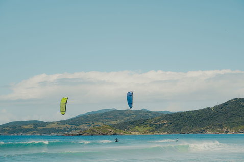 Duotone Juice LEI Kite beim Kitesurfen an der Meeresküste mit grünen Hügeln in türkisgrün und blau