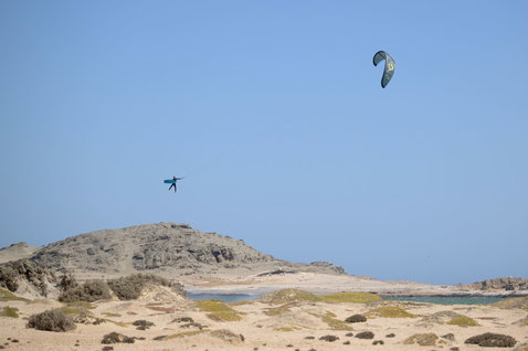 Duotone D/LAB LEI kite lors du kitesurf sur des dunes côtières arides avec cap rocheux et lagon