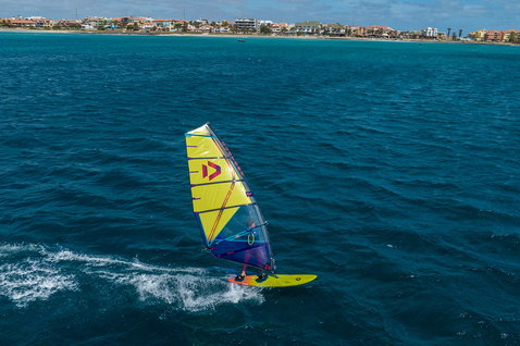 Duotone Ultra FreeWave D/LAB windsurf board during windsurfing on a coastal ocean with turquoise sea and beach town