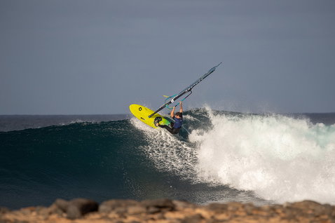 Planche de windsurf Duotone Grip [Tri] D/LAB lors du surf de vagues sur un rivage rocheux