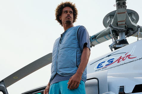 Veste sans manches matelassée Duotone Apparel Explore en bleu acier portée par un homme devant un hélicoptère