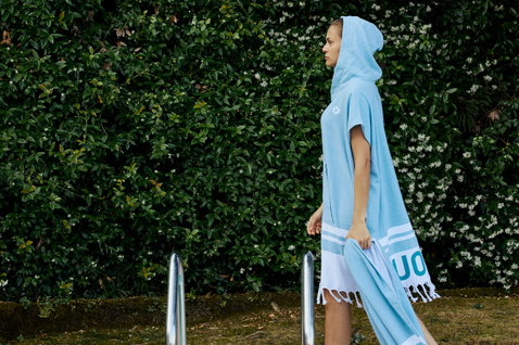 Duotone unisex hooded poncho in light blue worn poolside in a garden setting
