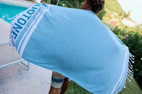 Serviette de plage Duotone Towel Logo en bleu ciel avec rayures blanches et franges au bord de la piscine