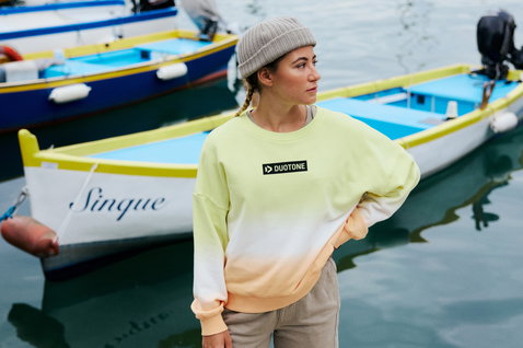 Duotone Seaman beanie en gris porté par une femme dans un port avec des bateaux colorés