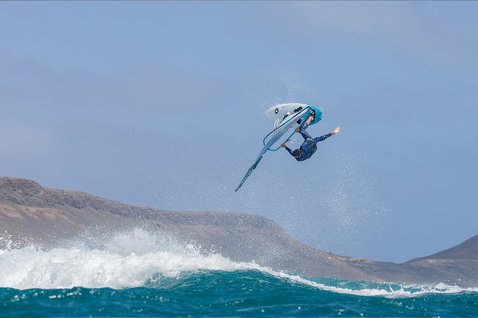 Duotone Grip [Quad] D/LAB windsurf board while wave riding on the ocean with rocky coastline