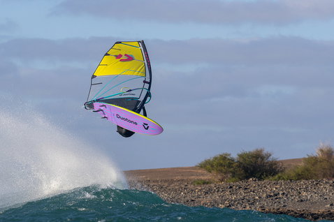 Duotone Grip [Tri] SLS windsurf board during wave riding at the ocean coast with rocky shoreline