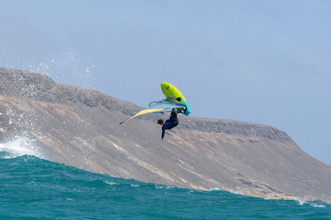 Duotone Grip [Tri] SLS windsurf board during wave riding at a rocky coastal hillside