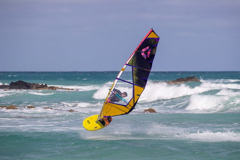 Duotone Ultra FreeWave SLS windsurf board during wave riding at a rocky ocean shore