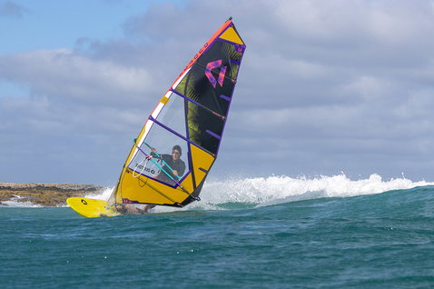 Duotone Ultra FreeWave SLS windsurf board during wave riding at ocean coastline with rocky shore