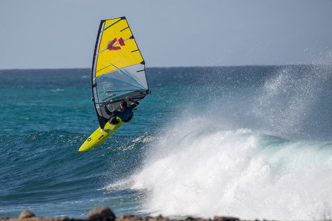 Duotone Ultra Grip [Quad] windsurf board during wave riding at a rocky ocean coastline