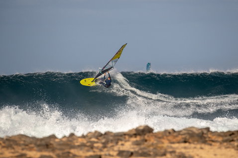 Duotone Ultra Grip [Quad] SLS windsurf board during wave riding at an ocean beach with rocky shore