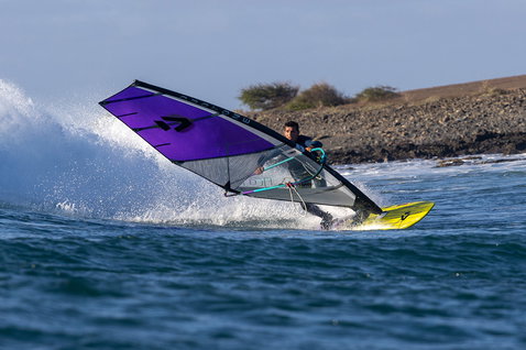 Duotone Ultra Grip [Quad] SLS windsurf board during wave riding at an ocean coastline with rocky shore