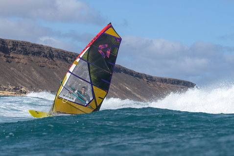 Duotone Duke Wave-Segel beim Wellenreiten an einem Ozeanstrand mit Felsklippen