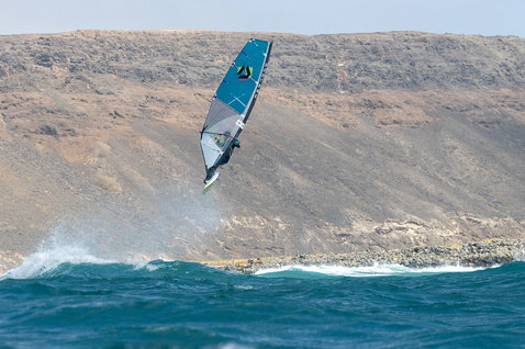 Duotone Super Hero D/LAB wave sail during wave riding at ocean coastline with rocky cliffs