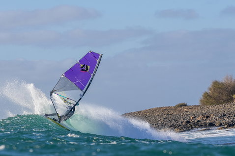 Duotone Super Hero D/LAB wave sail during wave riding at a rocky ocean coastline