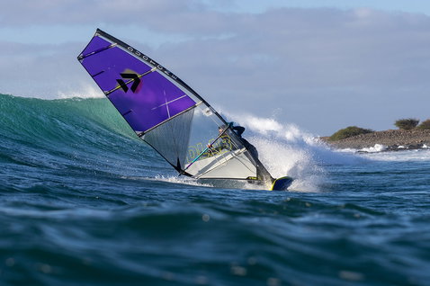 Duotone Super Hero D/LAB wave sail during wave riding at a rocky ocean coastline