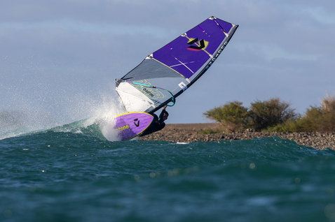 Duotone Super Hero D/LAB wave sail during wave riding on a rocky ocean coastline