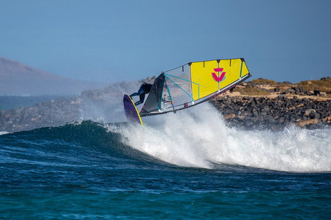 Duotone Super Hero SLS wave sail during windsurfing on the ocean coastline with rocky shore
