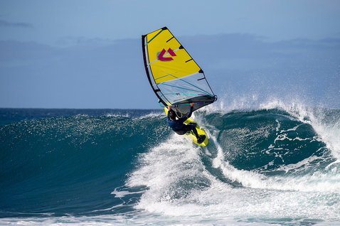 Duotone Super Hero SLS wave sail during wave riding at ocean beach in yellow-green, black and pink