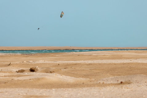 Duotone Trust Bar Quad Control barre de contrôle en train de faire du kitesurf sur une plage désertique avec océan