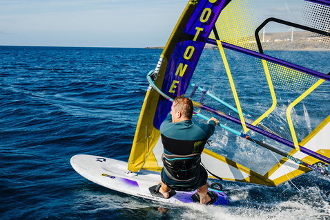 Duotone Falcon Fin D/LAB planche de windsurf lors du windsurf en mer avec côte rocheuse et éoliennes