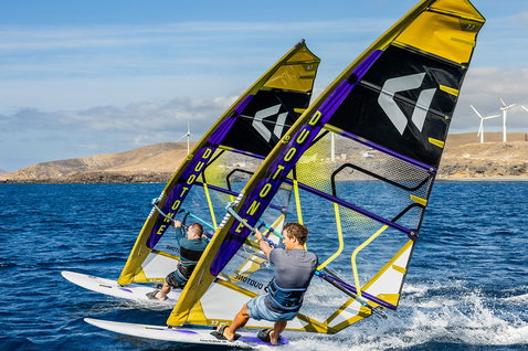 Duotone Warp Fin voile de course 7,7 m² lors du freeride sur eaux côtières avec panorama montagneux et éoliennes en bleu marine foncé