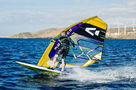 Duotone Warp Fin voile de course lors de la planche à voile sur océan ouvert avec collines côtières arides et éoliennes