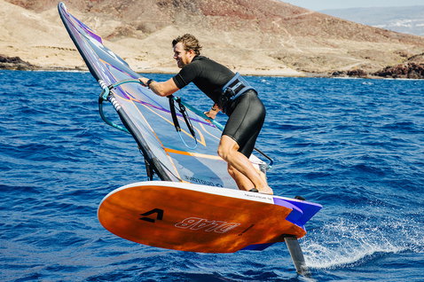 Duotone Falcon Foil D/LAB windsurf board while wing foiling in a rocky coastal ocean landscape